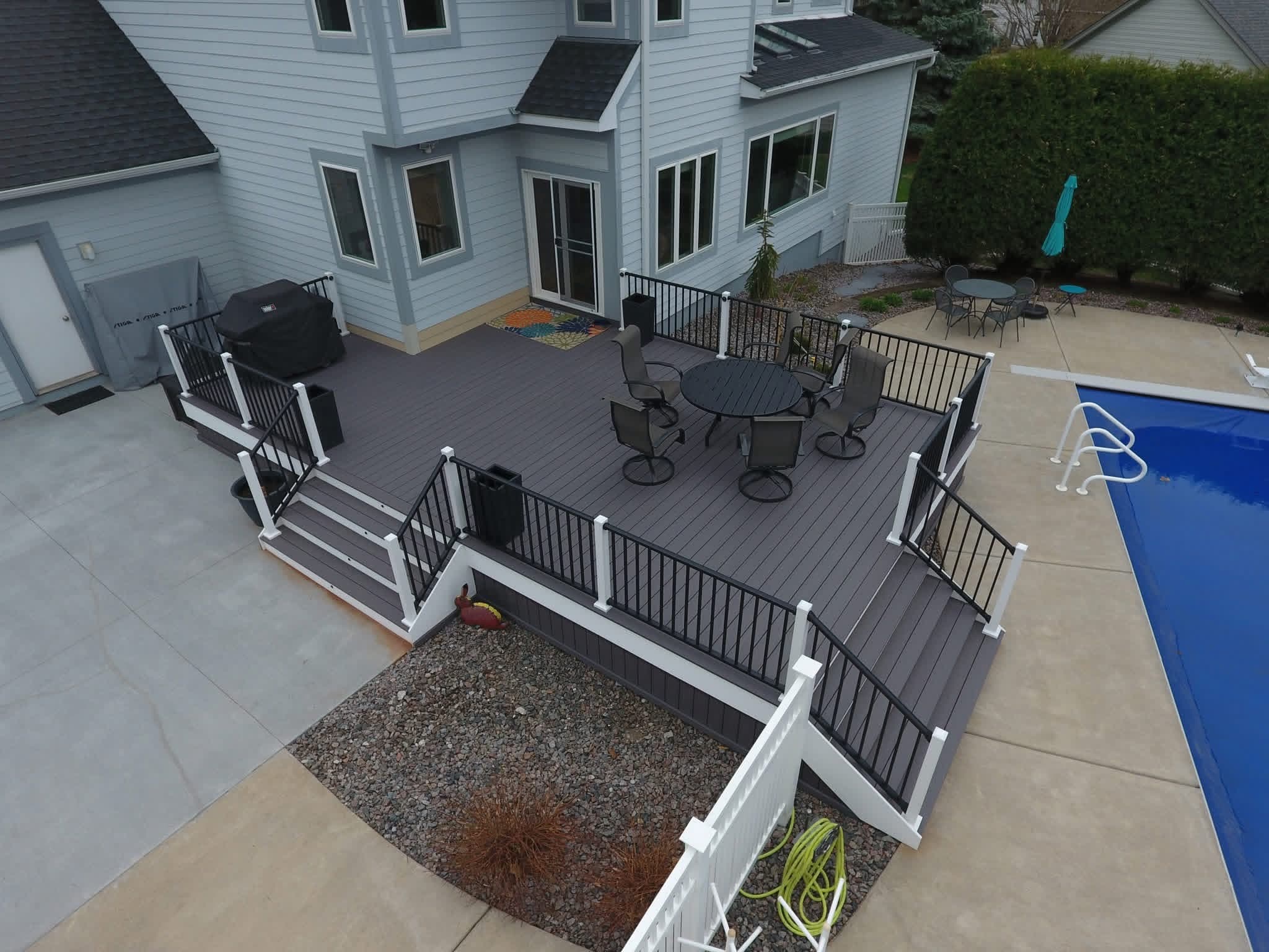 Dark deck with white posts wrapping a backyard pool and patio